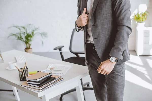 Обрезанный образ бизнесмена, стоящего в сером костюме и с наручными часами в офисе — стоковое фото