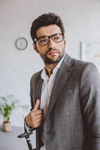 Guapo hombre de negocios en gafas mirando hacia otro lado en la oficina - foto de stock