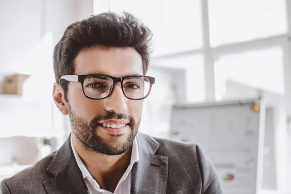 Porträt eines lächelnden gutaussehenden Geschäftsmannes mit Brille, der im Büro in die Kamera blickt — Stockfoto