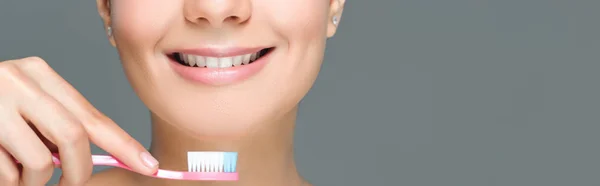 Cropped shot of smiling woman holding tooth brush in hand isolated on grey — Stock Photo