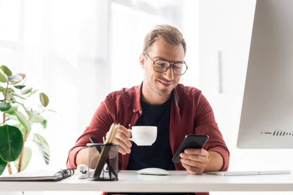 Uomo d'affari con tazza di caffè utilizzando smartphone in ufficio moderno — Foto stock