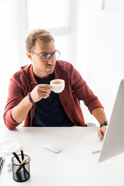 Businessman in glasses holding cup of coffee in modern office — Stock Photo