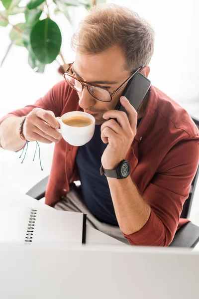 Casual businessman drinking coffee and talking on smartphone — Stock Photo