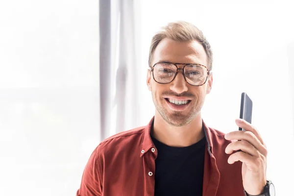 Homme heureux dans les lunettes tenant smartphone dans la main dans le bureau moderne — Photo de stock