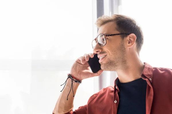 Bell'uomo in occhiali che parla su smartphone vicino alla finestra — Foto stock