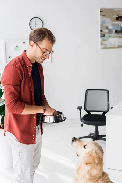 Mann füttert süßen Hund mit Futter aus Metallschale — Stockfoto