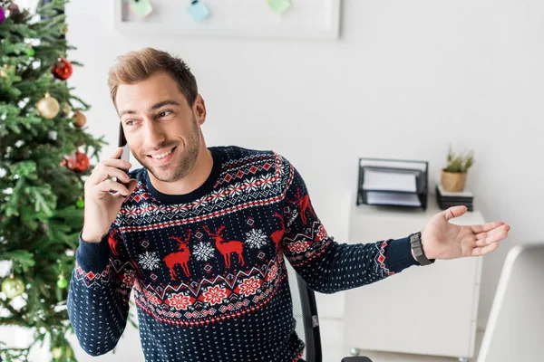 Smiling businessman in christmas sweater talking on smartphone in office — Stock Photo