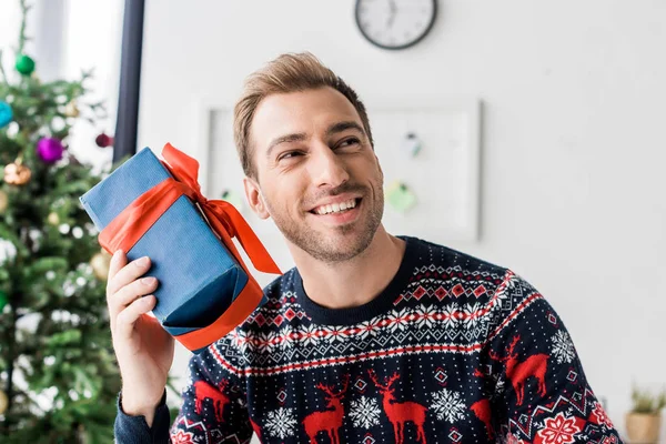 Smiling man in christmas sweater with present near head — Stock Photo