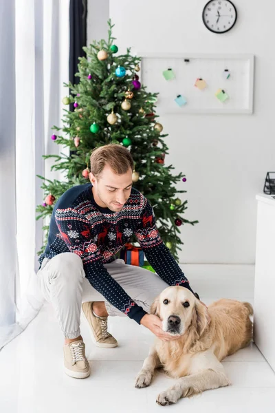 Man in christmas sweater stroking golden retriever dog — Stock Photo