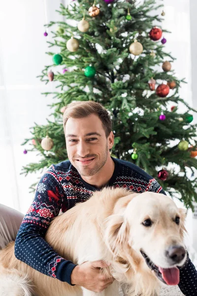 Smiling man in christmas sweater hugging golden retriever dog — Stock Photo