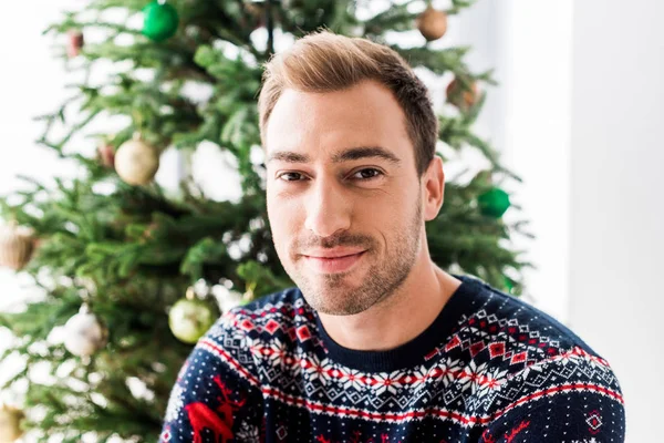 Людина в різдвяному светрі проти ялинки — стокове фото
