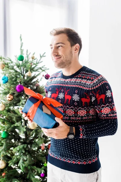 Усміхнений чоловік у різдвяному светрі з подарунковою коробкою — стокове фото