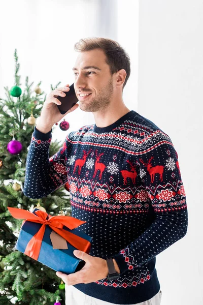 Man in christmas sweater with gift box talking on smartphone — Stock Photo