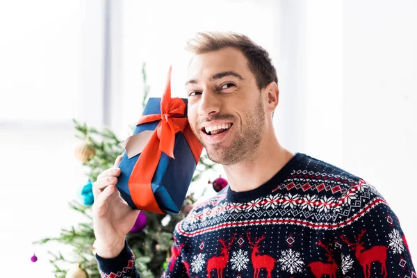 Smiling man in christmas sweater with gift box near head — Stock Photo