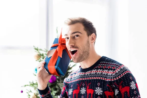 Uomo in maglione di Natale con scatola regalo vicino alla testa — Foto stock