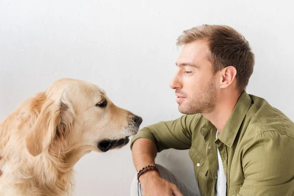 Golden retriever perro y hombre sentado contra la pared blanca - foto de stock