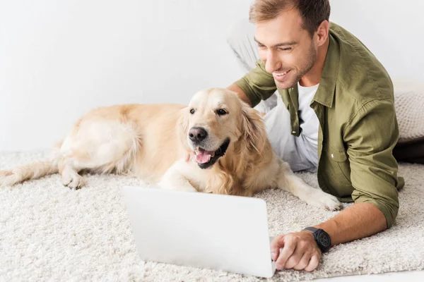 Man with golden retriever lying on floor and using laptop — Stock Photo