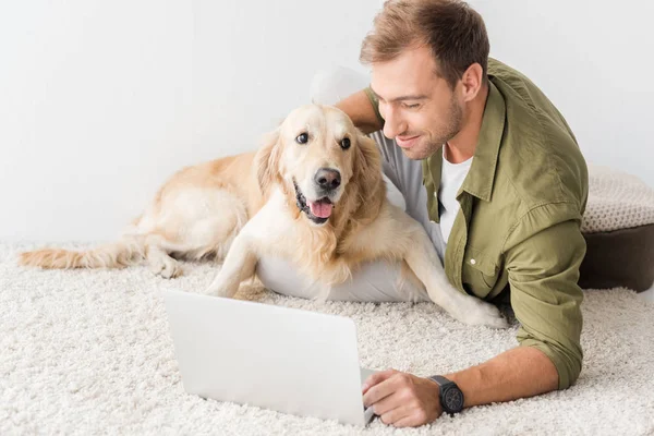 Man with dog lying on beige rug and using laptop — Stock Photo