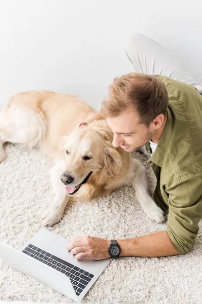 Hombre con perro acostado en el suelo y el uso de ordenador portátil - foto de stock