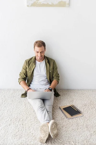 Freelancer casual usando laptop en alfombra beige - foto de stock