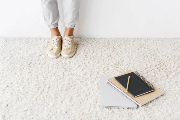 Cropped view of casual man standing on beige rug with laptop and notebooks — Stock Photo