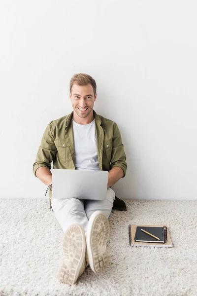 Freelancer sonriente usando laptop en alfombra beige - foto de stock