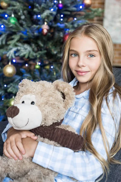 Schönes Kind hält Teddybär in der Hand und lächelt zur Weihnachtszeit in die Kamera — Stockfoto