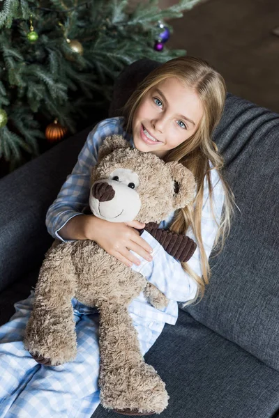 Vue grand angle d'adorable enfant heureux étreignant ours en peluche et souriant à la caméra à la période de Noël — Photo de stock