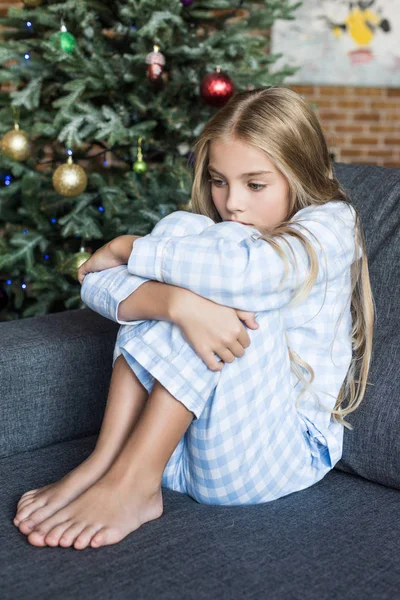 Upset kid in pajamas sitting on sofa at christmas time — Stock Photo