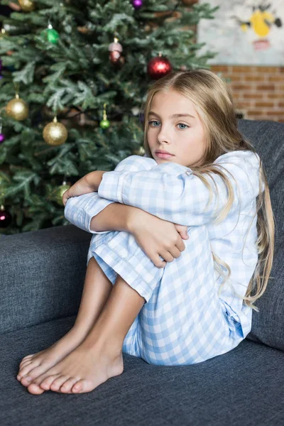 Upset child in pajamas sitting on sofa at christmas time — Stock Photo