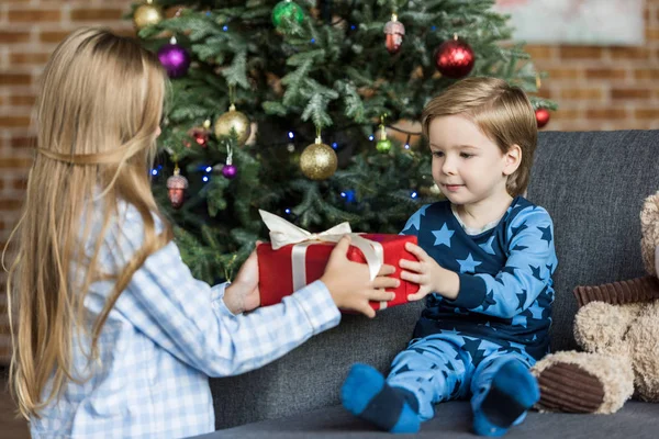 Adorable children in pajamas holding christmas gift at home — Stock Photo