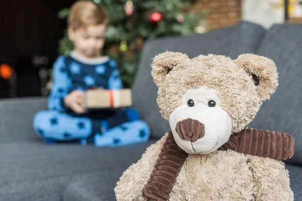 Vue rapprochée de l'ours en peluche et de l'enfant tenant un cadeau de Noël derrière lui — Photo de stock