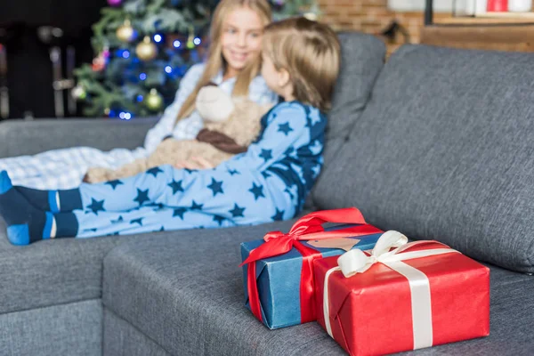 Vista da vicino dei regali di Natale e dei bambini in pigiama seduti sul divano dietro — Foto stock