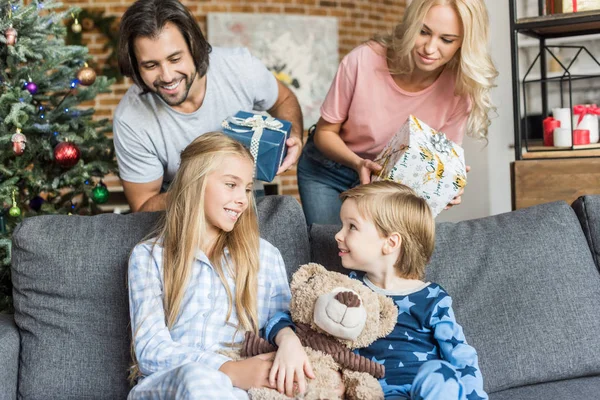 Parents presenting christmas gifts to adorable happy children in pajamas — Stock Photo