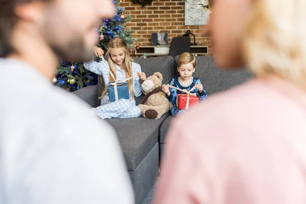 Focus selettivo dei genitori sui bambini in primo piano e felici in pigiama apertura regali di Natale — Foto stock