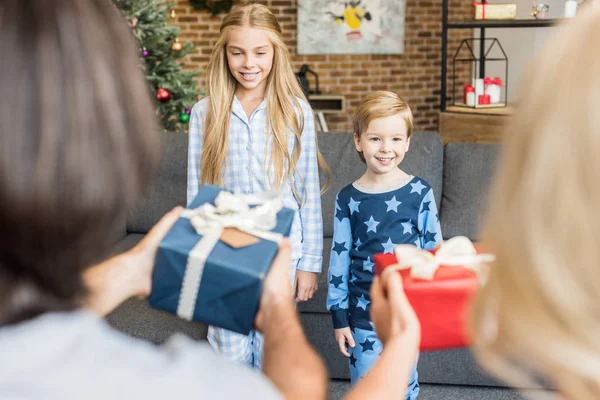 Foyer sélectif des parents présentant des cadeaux de Noël aux enfants heureux en pyjama — Photo de stock