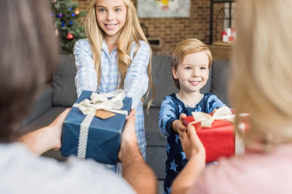 Schnappschuss von Eltern, die glücklichen Kindern Weihnachtsgeschenke im Pyjama präsentieren — Stockfoto