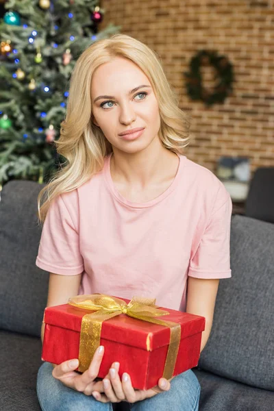 Красивая молодая блондинка, держащая в руках подарок и отводящая взгляд от дома — стоковое фото