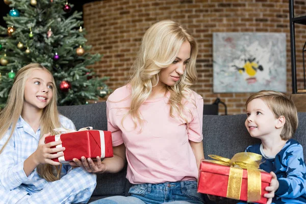 Sorrindo jovem mãe apresentando presentes de Natal para crianças felizes em pijama — Fotografia de Stock