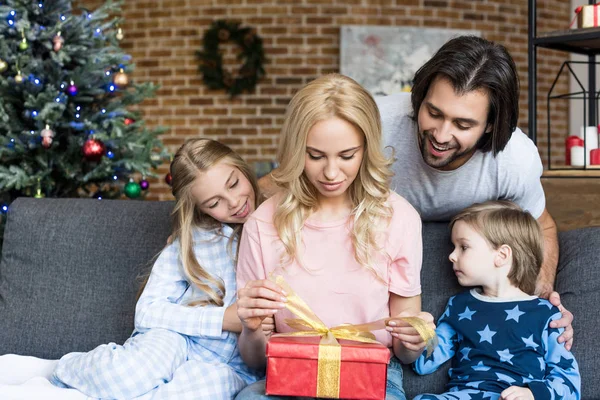 Heureux père avec deux adorables enfants regardant mère ouverture cadeau de Noël à la maison — Photo de stock