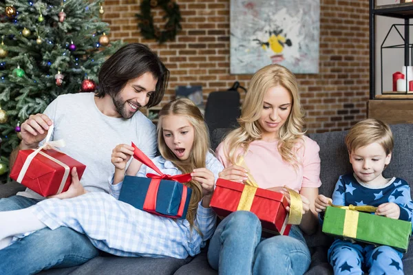 Familia feliz con dos adorables niños abriendo regalos de Navidad juntos - foto de stock