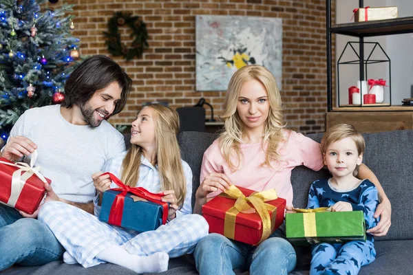 Belle famille heureuse avec deux enfants tenant des cadeaux de Noël et assis ensemble à la maison — Photo de stock