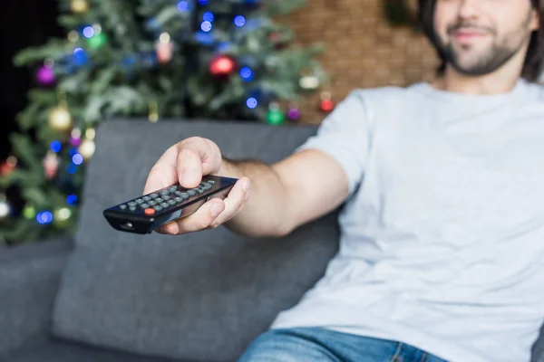 Vista close-up do homem usando controlador remoto enquanto sentado no sofá no Natal — Fotografia de Stock