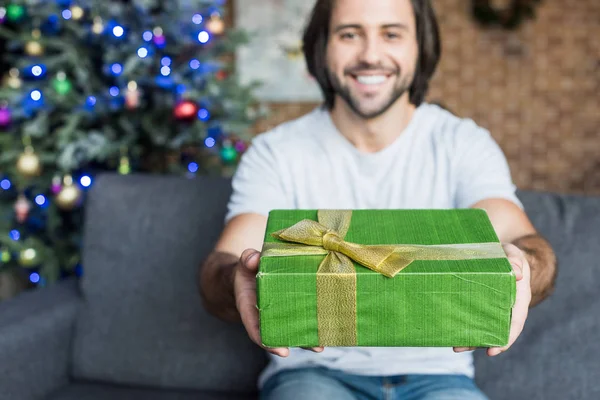 Happy young man holding christmas present and smiling at camera — Stock Photo