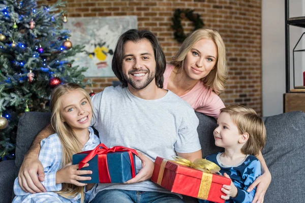 Щасливі батьки і милі діти в піжамах тримають різдвяні подарунки і посміхаються на камеру — стокове фото