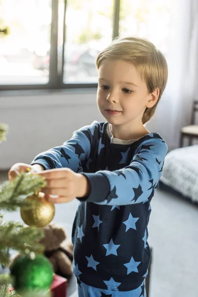 Carino sorridente bambino in pigiama decorare albero di Natale — Foto stock