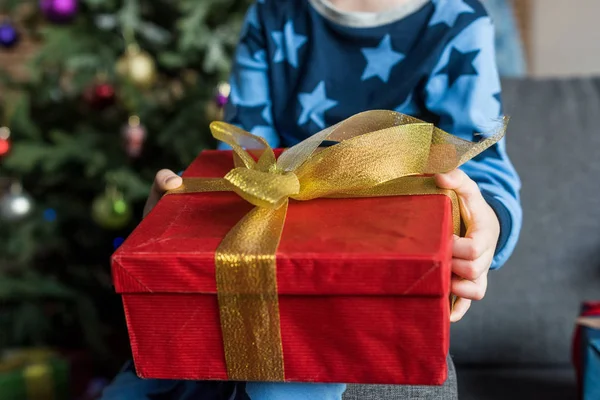 Nahaufnahme des Kindes im Pyjama, das auf der Couch sitzt und ein Weihnachtsgeschenk in der Hand hält — Stockfoto