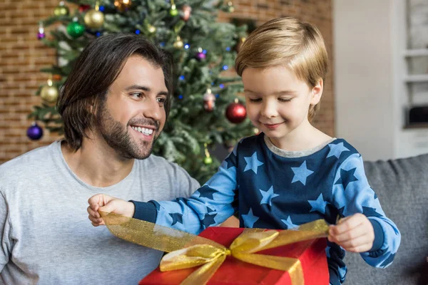 Feliz padre mirando adorable pequeño hijo abriendo regalo de Navidad - foto de stock
