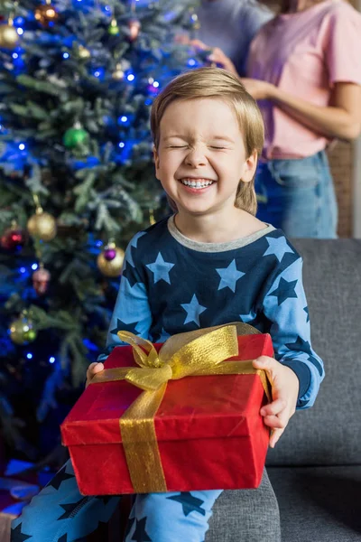 Cheerful little boy in pajamas holding christmas present — Stock Photo