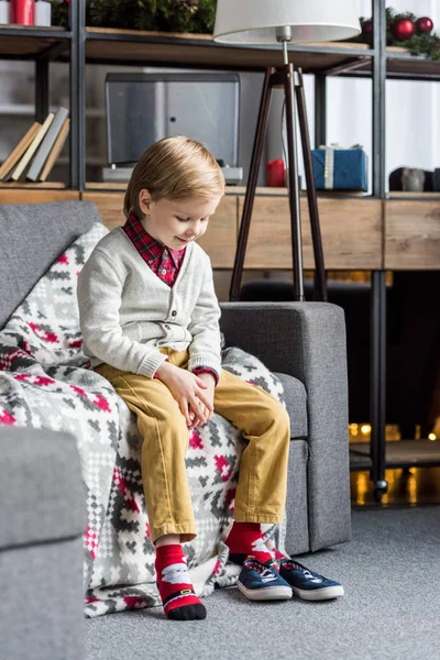 Adorable enfant heureux assis sur le canapé et regardant des chaussures — Photo de stock